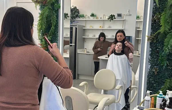 Salão da clínica com jardim vertical, espelho iluminado e uma cliente sendo atendida
